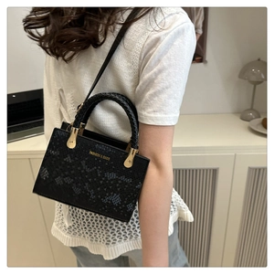Detail of black faux leather handbag with stone pattern and woven handles on a model