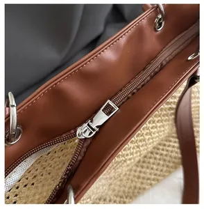 Detailed close-up of smooth silver metal zipper on woven straw and brown leather tote bag