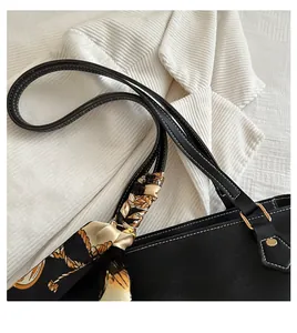 Close-up of black leather tote bag handle with elegant printed silk scarf and gold hardware