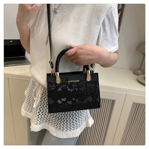 Close-up of black snakeskin texture handbag with gold fashion lettering and woven handle