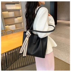Detailed view of black tote bag with elegant striped scarf on handle in home setting