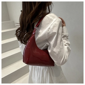 Détail d'un sac demi-lune en cuir verni bordeaux porté par un mannequin chic