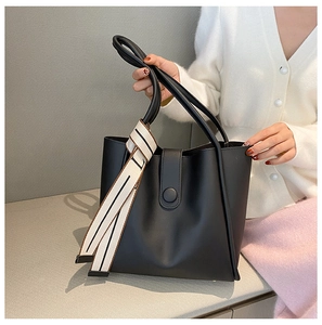 Detail of black tote bag featuring matte faux leather texture and decorative silk scarf
