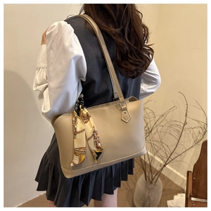 Detail view of a beige tote bag with decorative silk scarf on a model's shoulder
