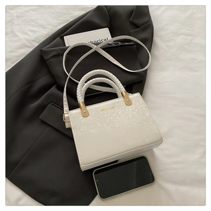 Close-up of cream crossbody bag with stone texture, woven handle and gold fashion lettering