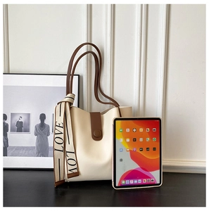 Detail view of a creamy white leather tote bag featuring brown handles and a decorative silk scarf