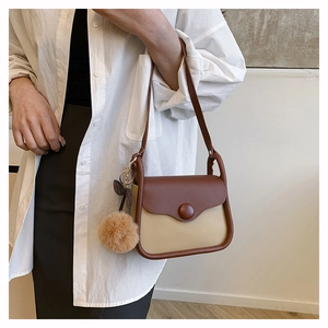 Detail of minimalist two-tone crossbody bag with round button and fuzzy pompom charm