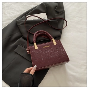 Detail of burgundy stone pattern square bag with woven handles and gold logo