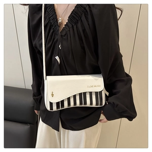 Détail du sac bandoulière touches de piano avec slogan doré et emblème de clé de sol