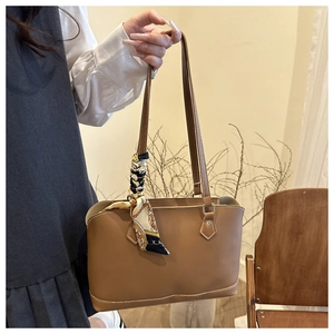 Close-up of a brown leather tote bag with a baroque silk scarf tied to the handle