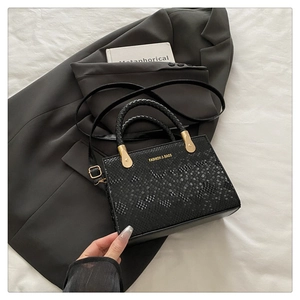 Detail of black faux snake pattern handbag with gold hardware and woven handle on a blazer