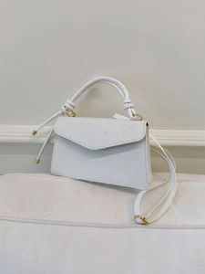 Détail du cuir blanc à motif autruche et des finitions métalliques dorées sur le sac