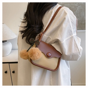 Detail of the brown and beige patchwork crossbody bag with plush ball and butterfly charms