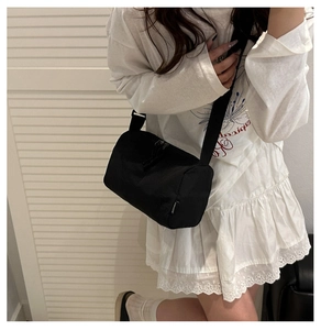 Detail of black cylindrical canvas crossbody bag with adjustable strap and double zippers