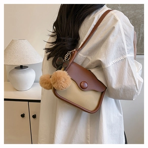 Close-up of beige canvas crossbody bag with brown leather trim and fluffy charm