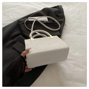 Detailed view of white faux snake pattern handbag with woven handle and gold hardware