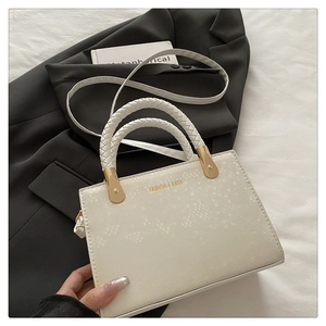 Close-up of white crossbody bag with stone texture and gold lettering on black jacket