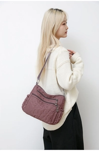 Model wearing a dark purple nylon shoulder bag with heart quilting and multiple pockets