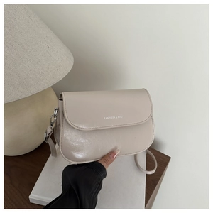 Détail du sac de selle beige clair avec logo argenté sur table en bois sombre