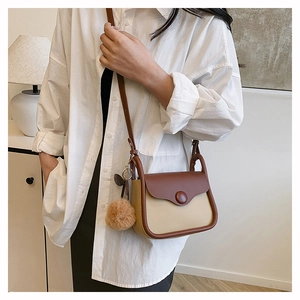 Close-up of contrast color crossbody bag with a plush charm worn on a model's shoulder