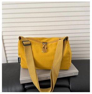 Detail of mustard yellow fabric crossbody bag with wide adjustable strap and brand tag