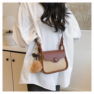 Detail view of a two-tone crossbody bag with beige and brown leather and pom-pom charm