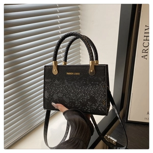 Detail of black faux leather crossbody bag with snake texture and gold hardware details