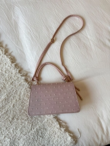 Gros plan d'un sac à main rose texturé avec broderie et boucles dorées sur lit moelleux