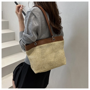 Detail of woven straw tote bag with brown leather handles worn by a model in a minimal setting