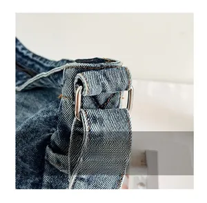 Detailed macro view of metal D-ring buckle and reinforced stitching on denim bag strap