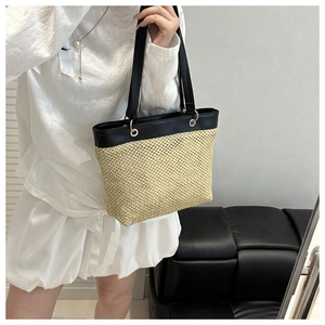 Detail of woven straw tote bag featuring black leather straps and silver metal rings