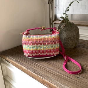 Dettaglio borsa tessuta colorata con tracolla in pelle rosa su base in legno retro