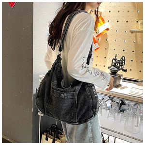 Detail of a black washed denim hobo bag featuring a side pocket with metal buckle