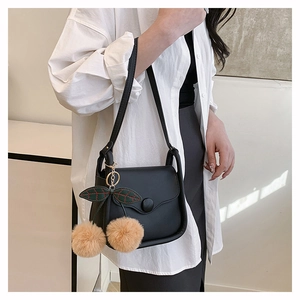 Detail of black leather shoulder bag featuring a cute plush cherry charm on the side