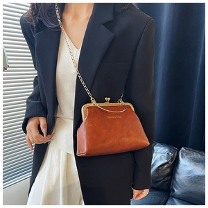 Dettaglio borsa vintage marrone con chiusura a scatto e catena oro indossata su un blazer