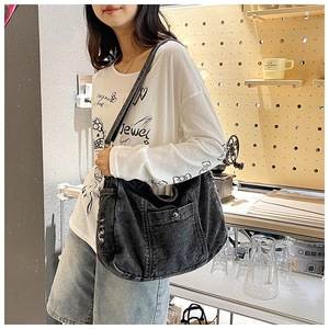 Detail of black denim hobo bag featuring front buckle pocket and adjustable strap