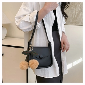 Detail of black matte shoulder bag featuring a decorative plush cherry charm and round clasp