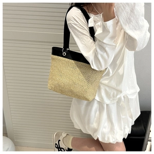 Detail of woven straw tote bag featuring black leather trim and wide shoulder strap