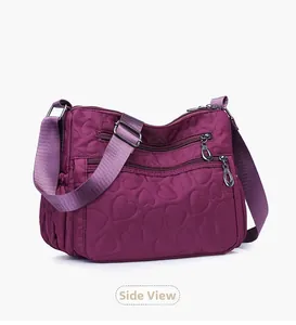 Detail view of purple heart-quilted nylon crossbody bag with multi-zipper pockets