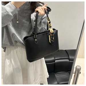 Detail of black leather tote bag featuring white contrast stitching and a decorative silk scarf