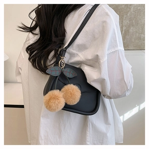Detail view of a black leather crossbody bag featuring a cute plush cherry charm on a model