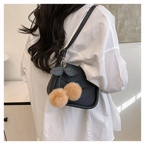 Detail of a black crossbody bag with unique cherry-shaped plush keychain and metal chain ring