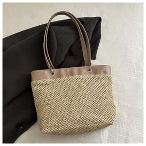 Detailed top view of a woven straw tote bag with khaki leather handles on linen cloth