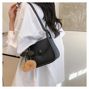 Detail of black saddle bag with decorative fur balls and leaf pendant on a white shirt