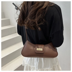 Close-up of brown baguette bag with golden buckle on female model in stylish setting