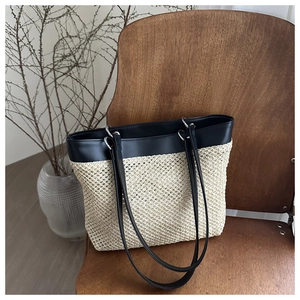 Detailed view of woven straw tote bag with black leather trim on a wooden chair