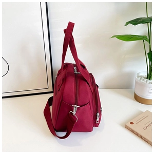 Détail d'un sac en toile bordeaux à poches multiples avec ferrures argentées et bandoulière
