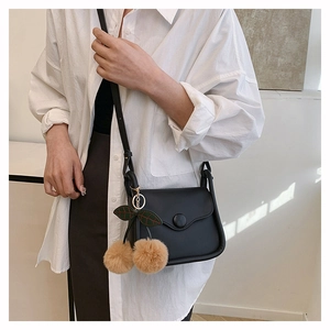 Detail of black leather crossbody bag with decorative round buckle and cherry pompom charm