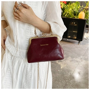 Dettaglio borsa vintage in pelle bordeaux con catena dorata su abito bianco