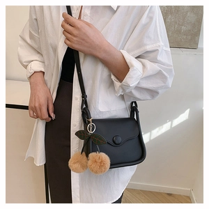 Detail of a black leather flap crossbody bag with decorative cherry pom-pom charms